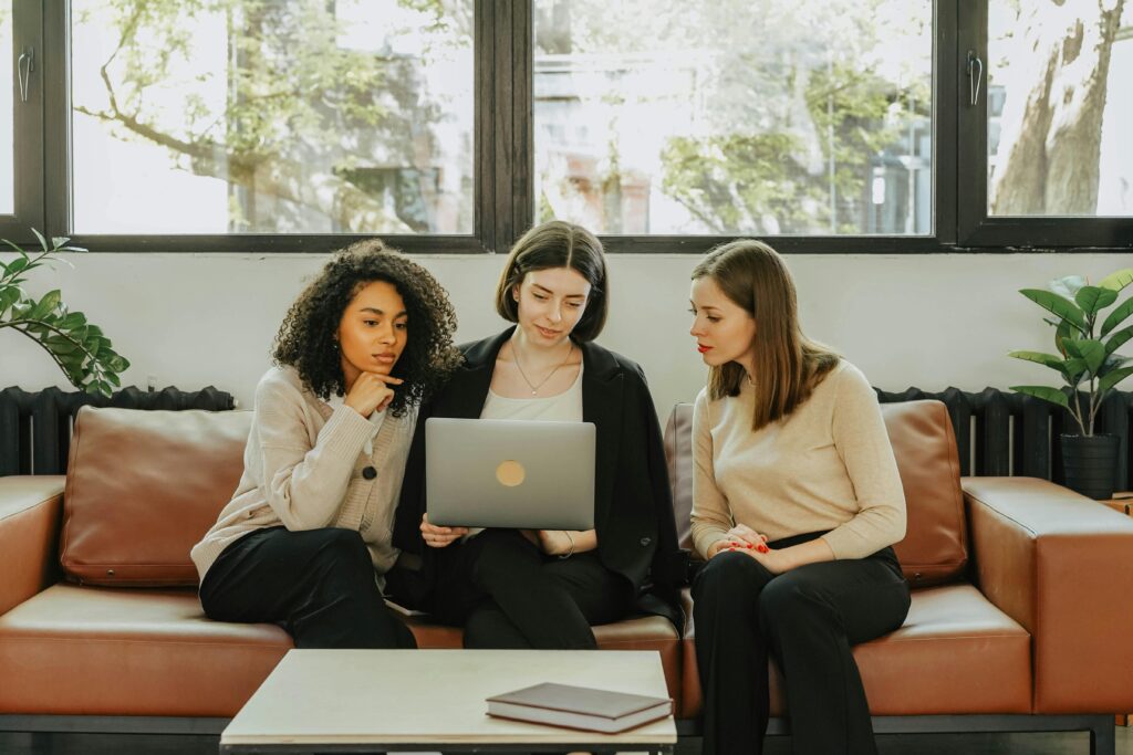 Three women seated on a couch looking at a laptop screen, discussing the lead generation funnel.